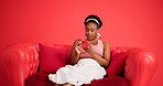 Phone, relax and black woman on sofa in studio with texting, chatting or social media on mobile app. Calm, technology and African female person with cellphone for contact online by red background.