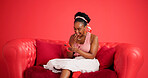 Studio, phone and black woman with surprise on sofa, gossip or announcement on social media. Smile, mobile and person on couch with shock, wow or reading news with notification on red background