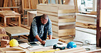 Black man, carpenter and typing with laptop at factory, notes and manufacturing report at industrial plant. Mature person, computer and technician with review, material and production at warehouse