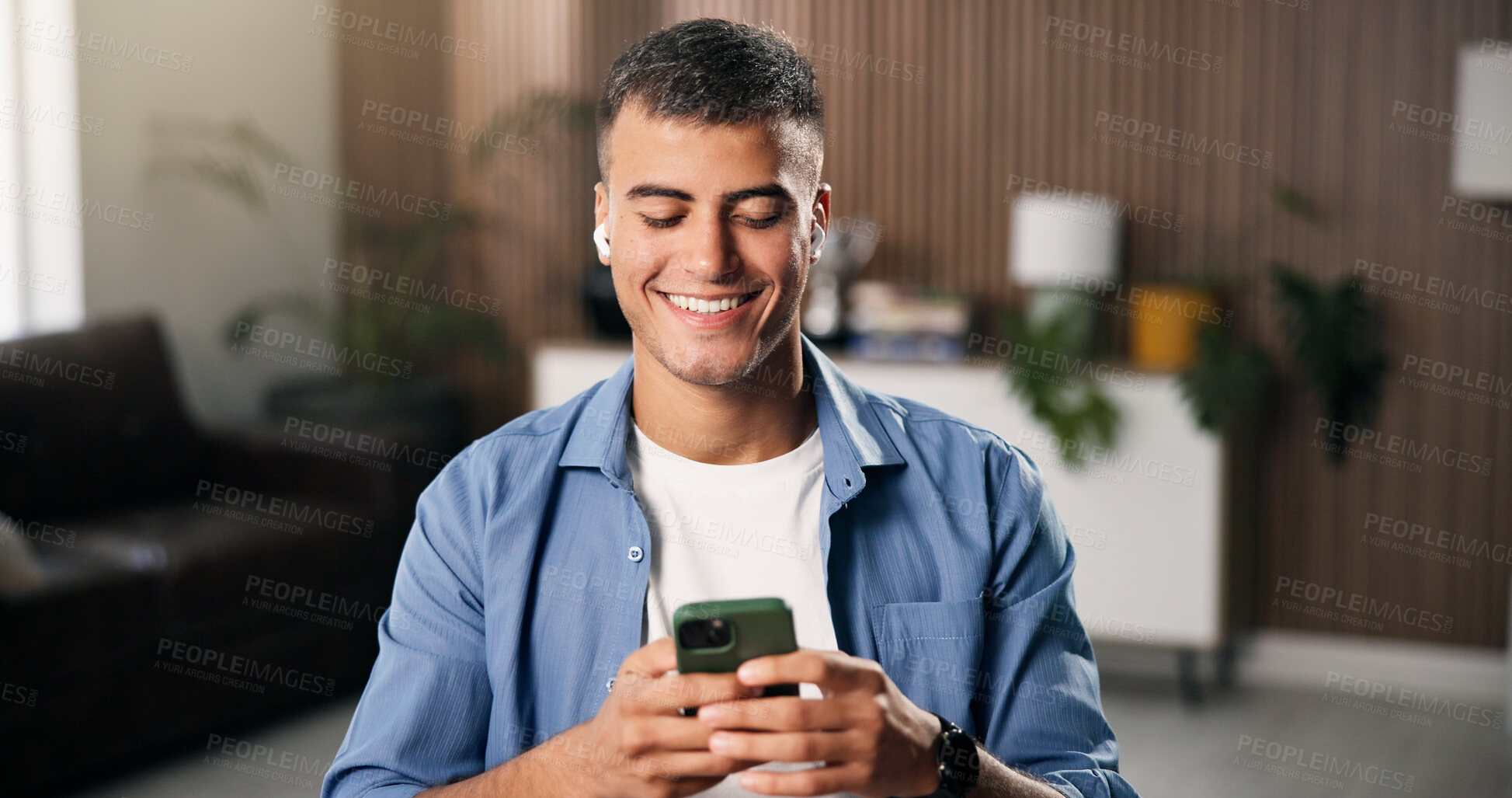 Buy stock photo Man, smile and earphones in living room with phone, watch social media video or typing text message. Happy, person relax and reading in home with audio tech, online chat and listen to music playlist.