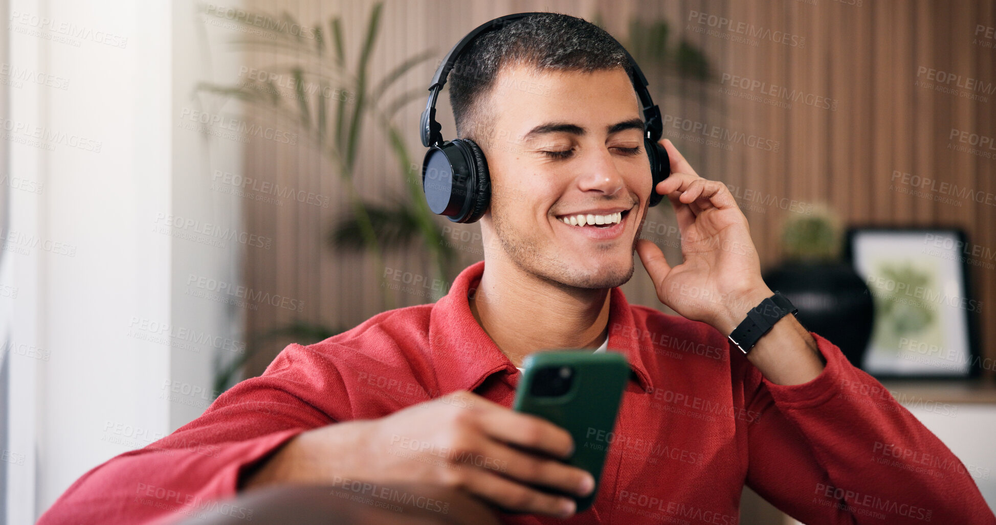 Buy stock photo Happy man, headphones and phone on sofa in home for audio, streaming service and relax in living room. Person, smartphone and listen to music with smile, subscription and scroll for song at apartment
