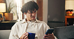 Coffee, confused and man on sofa with phone for social media, online message and chat in home. Weekend, gossip and person with tech for rumor, fake news and notification on mobile app with drink