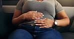 Hands, stomach ache and woman in home with pain, endometriosis or menstrual cramps on sofa. Living room, sore abdomen and sick person with constipation, food poisoning and bloated with gas in house