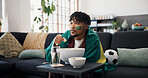 Man, sports and popcorn on sofa with Brazil flag, watching tv or support national team for football. Black person, eating snack and broadcast in home with soccer world cup, tournament or live stream.