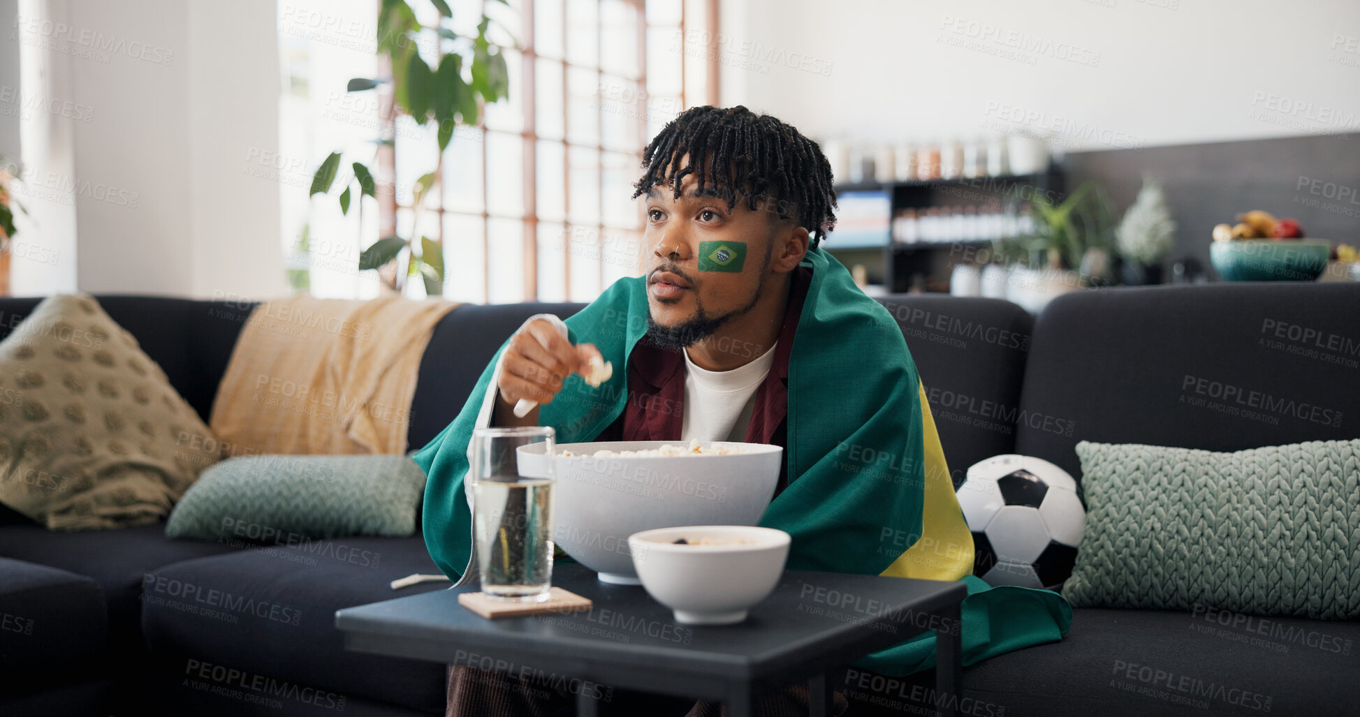 Buy stock photo Man, sports and popcorn on sofa with Brazil flag, watching tv or support national team for football. Black person, eating snack and broadcast in home with soccer world cup, tournament or live stream.