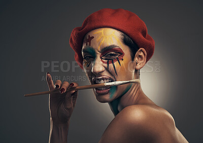 Buy stock photo Portrait, woman and face paint in studio with paintbrush, beret and creativity for artistic expression. Person, bite art tool and bold makeup with unique aesthetic, hat or texture on gray background.