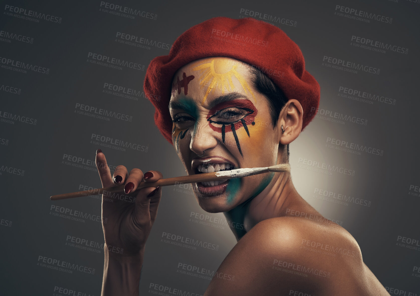 Buy stock photo Portrait, woman and face paint in studio with paintbrush, beret and creativity for artistic expression. Person, bite art tool and bold makeup with unique aesthetic, hat or texture on gray background.