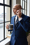Businessman talking on smartphone looking out window having phone call conversation in office holding coffee