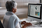 Mature business woman using computer with financial graph data on screen working in office