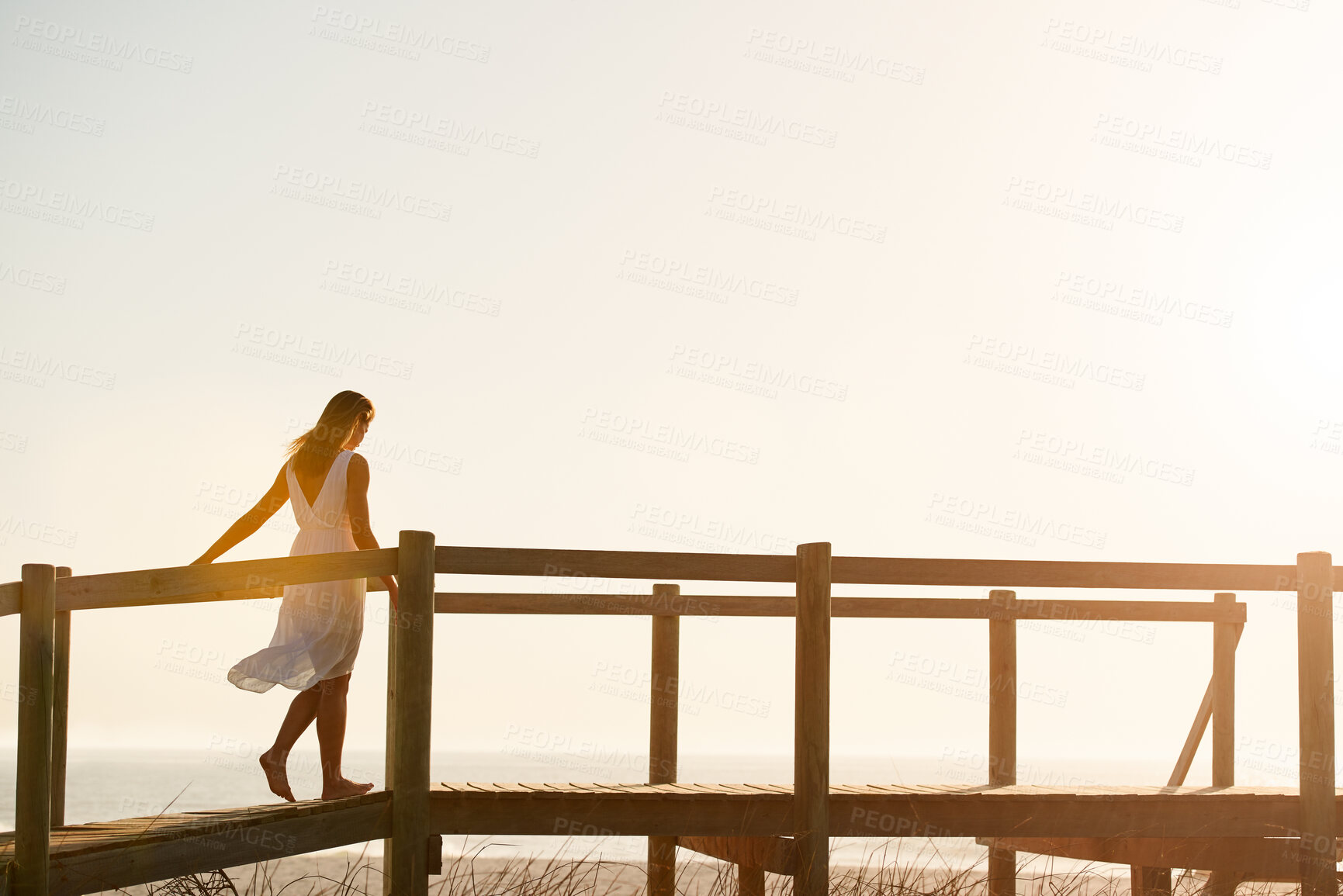 Buy stock photo Woman, walking or bridge with sunset on beach for outdoor freedom, travel or summer vacation. Female person, sunshine and adventure on wooden crossing or space for holiday or weekend getaway by ocean