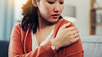 Shoulder, pain and Asian woman on sofa with injury for fibromyalgia, osteoporosis and inflammation. Home, upset and person massage arm for strain, muscle tension and joint ache in living room