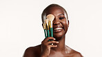 Portrait, smile and black woman in studio with makeup brush, wellness and product for beauty routine. Happy, female person and cosmetic tools for grooming, self care or foundation on white background