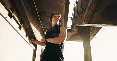 Buy stock photo Stretching, fitness and man in city with headphones for exercise, workout and ready for training. Low angle, outdoor and person with muscle warm up for mobility, health and active hobby with music