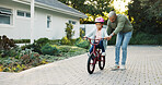 Balance, development and father teaching daughter how to ride bicycle outdoor in front of home. Guide, helping and single parent of girl child in driveway for cycling activity, growth or learning
