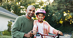Portrait, smile and father teaching daughter how to ride bicycle outdoor in front of home. Development, helmet and safety of girl child with single parent man in driveway for cycling or learning