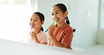 Girls, sisters and brushing teeth with toothbrush by mirror in bathroom, oral hygiene or morning routine. Reflection, grooming and happy children with dental care for wellness, cleaning mouth or home