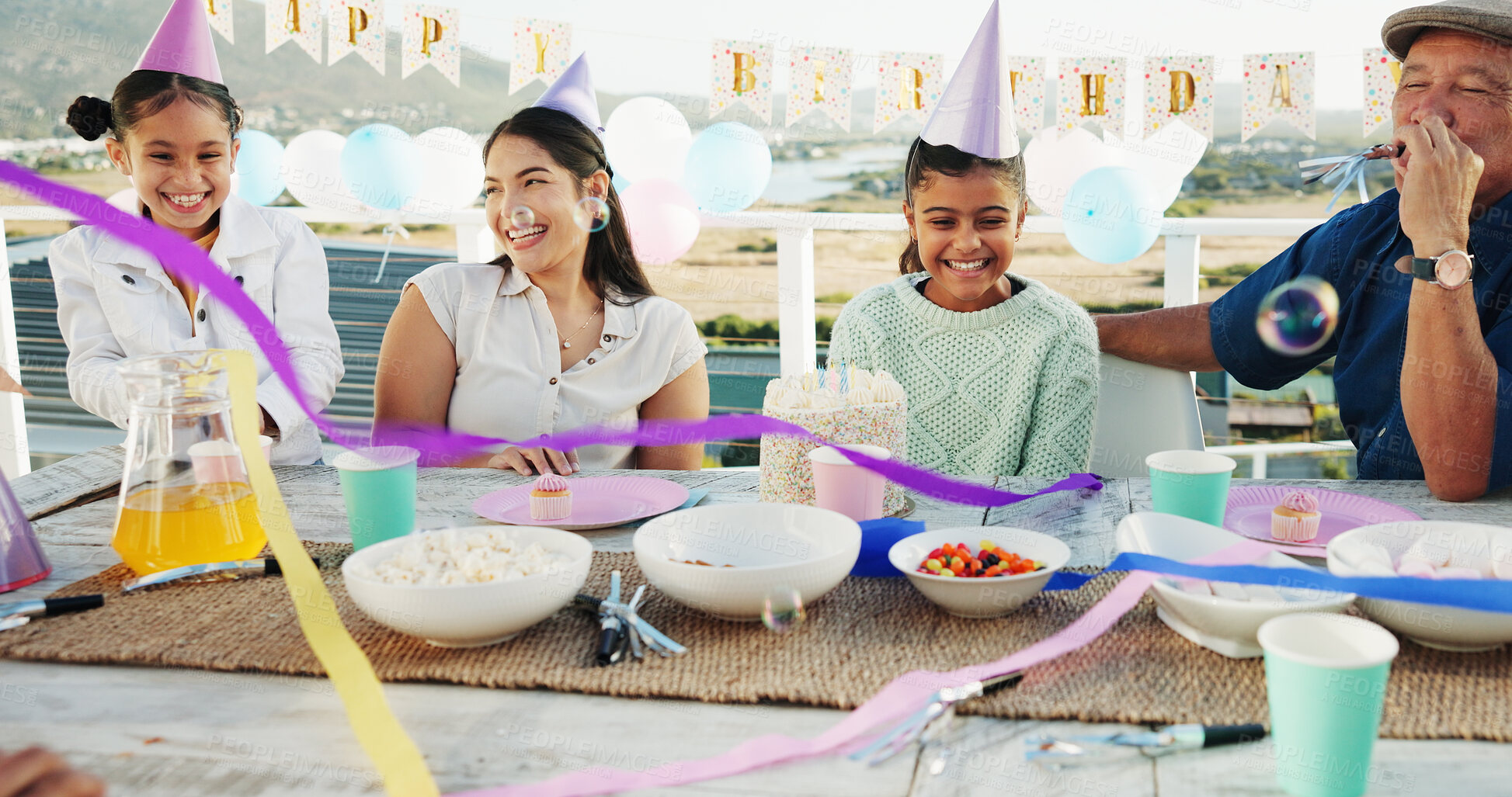 Buy stock photo Family, laugh and children at birthday party with cake, snacks and generations bonding in backyard. Happy, people and girls outdoor on balcony with mother, grandfather and decoration for celebration.