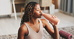 Yoga, woman and drinking water in house with rest, wellness or natural detox for holistic health. Thirsty, black person and exercise break in apartment with bottle, fitness or beverage for hydration.