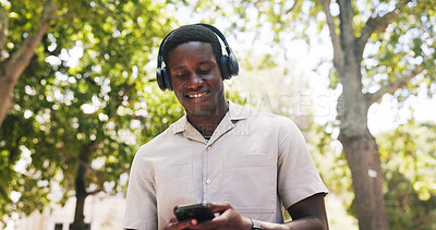 Buy stock photo Black man, phone and smile at park with headphones, streaming or listen to music with low angle in summer. African person, happy and outdoor with mobile app, sound or audio subscription in nature