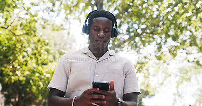 Buy stock photo Black man, phone and music at park with headphones, streaming or listen to sound with low angle in summer. African person, scroll and outdoor with mobile app, texting or audio subscription in nature