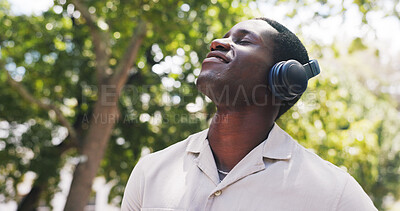 Buy stock photo Black man, thinking and happy at park with headphones, streaming or listen to music on commute in summer. African person, smile and tourism with sightseeing, sound or audio subscription in nature