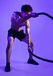 Man, battle ropes and fitness in studio for training, muscle and challenge on purple background. Person, cord and sweat with intense workout, exercise and power with endurance for cardio wellness