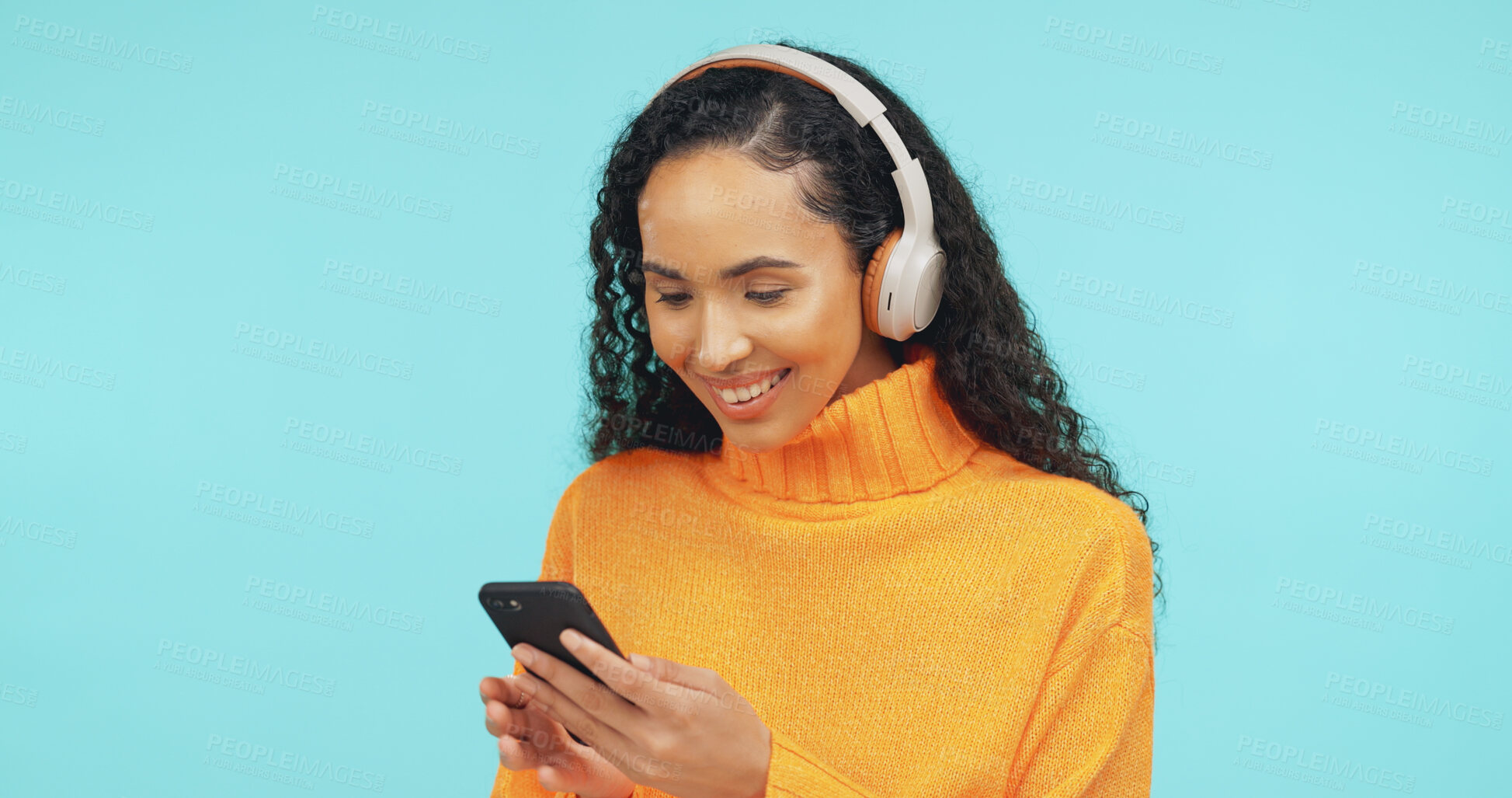 Buy stock photo Happy, phone and woman with headphones in studio for online streaming, music app and subscription. Space, typing and person on smartphone listening to audio, radio and playlist on blue background