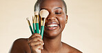 Makeup, happy and woman with cosmetic brushes for beauty, natural makeover and confidence. Cosmetology, black person and laughing with tools on studio background for skincare, foundation or skin glow