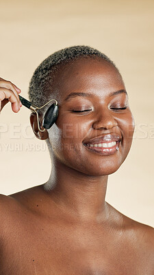 Buy stock photo Black woman, beauty and smile with facial roller for self care, natural skincare and lymphatic drainage. Massage, glow and circulation benefits on studio background for wellness, dermatology and tool
