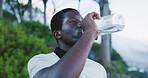 Black man, fitness or drinking with water in nature for outdoor workout break, rest or recovery. Active, male person or hiker with mineral liquid, bottle or beverage for thirst, hydration or vitamins