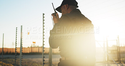 Buy stock photo Security, man and outdoor with radio for communication, surveillance and guard by fence with flare. Protection, service and back of person with tech for safety, perimeter search or patrol at sunset