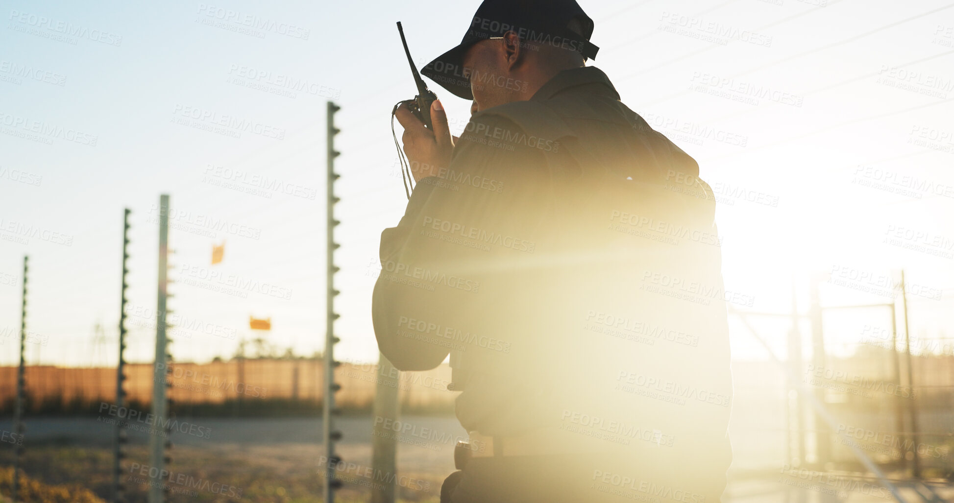 Buy stock photo Security, man and outdoor with radio for communication, surveillance and guard by fence with flare. Protection, service and back of person with tech for safety, perimeter search or patrol at sunset