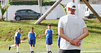 Outdoor, children or man with coaching for football, sports training or instructions for practice match. Fitness, soccer club or coach with kids team for skill development, field or explain exercise