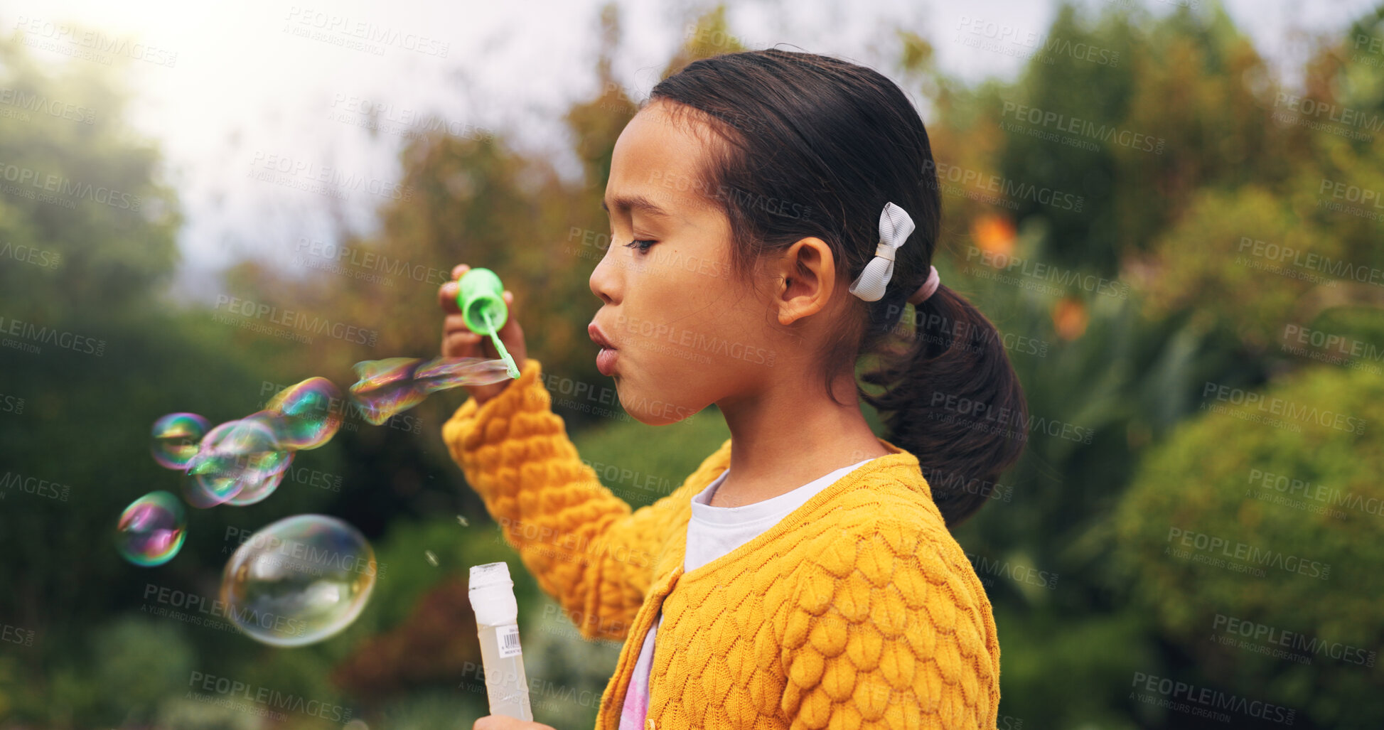 Buy stock photo Outdoor, child and blowing bubbles in nature, growth and development with activity on weekend break. Park, entertainment and girl with toy for soap balloons, fine motor skills or playing game for fun