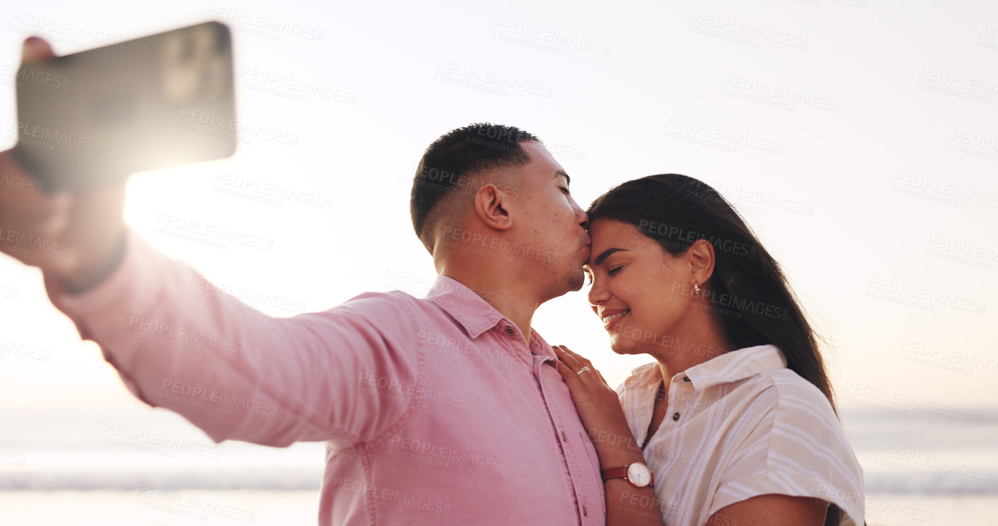 Buy stock photo Selfie, kiss and couple at beach with sunrise for travel memory, social media and bonding on weekend. Marriage, love and photo of man and woman by ocean for relationship, picture and post on holiday
