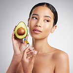 A gorgeous mixed race woman holding an avocado and syringe. Hispanic model promoting the skin benefits of avocado extract against a grey copyspace background