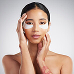 Studio Portrait of a beautiful mixed race woman wearing under eye patches. Hispanic model with glowing skin using hydrating treatment against a grey copyspace background