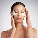 A young beautiful mixed race woman wearing under eye patches. Hispanic model with glowing skin using hydrating treatment against a grey copyspace background