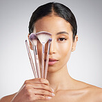 Studio Portrait of a beautiful mixed race woman posing with a collection of makeup brushes during pamper routine. Hispanic model with cosmetic tools standing against a grey copyspace background