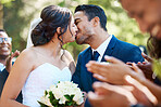 Happy romantic newlywed couple kissing outside while surrounded by friends and family on their wedding day. Bride and groom deeply in love