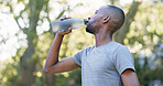 Fitness, man and drinking water for thirst at park with cardio break, runner recovery and nutrition. Athlete, black person and beverage in nature for exercise electrolytes, hydration or healthy detox