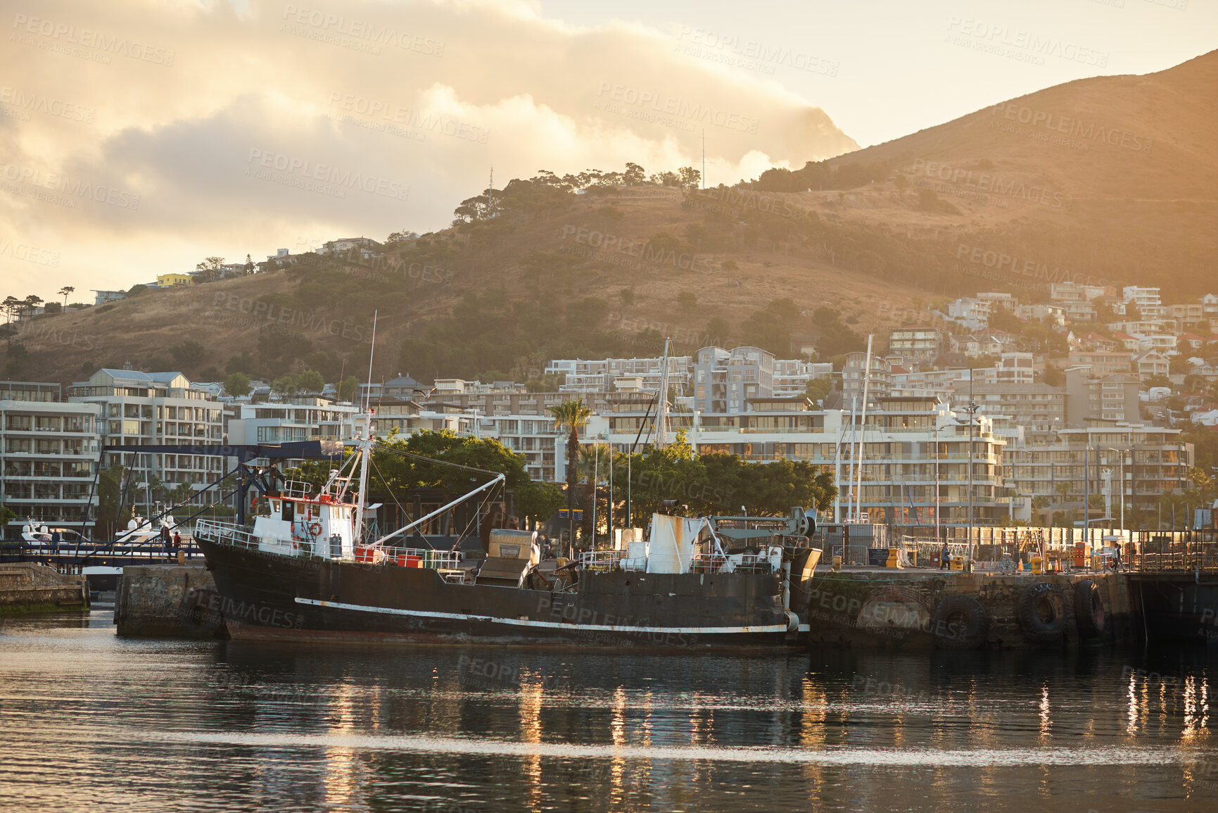 Buy stock photo Outdoor, sea and boat in city with harbor, travel destination and buildings for urban development. Mountain, ocean and fishing vessel in port with coastal town, sunset or scenic for tourist vacation.