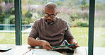 Man, reading and documents in home with tablet, financial planning or online website for utility bills. Mature, black person and glasses in house with tech, paperwork or budget for household expenses