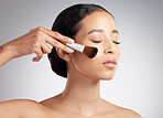 A beautiful mixed race woman posing with a makeup brush during a pamper routine. Hispanic model holding a contouring brush against a grey copyspace background