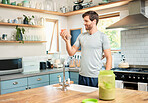 One fit young caucasian man drinking bottle of chocolate whey protein shake for energy for training workout while wearing earphones in a kitchen at home. Guy having nutritional sports supplement for muscle gain and dieting with weightloss meal replacement