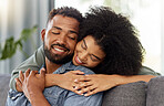 Young happy mixed race couple embracing while relaxing at home. Hispanic boyfriend and girlfriend smiling while hugging in the lounge at home