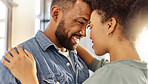 Young happy mixed race couple hugging while relaxing at home. Cozy hispanic husband and wife smiling while staring into each other&rsquo;s eyes lovingly and hugging in the lounge at home