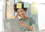 Young happy mixed race woman on a call with her phone while working a laptop sitting at a table at home. One cheerful hispanic female with a curly afro talking on the phone and sending an email on a laptop alone in the lounge at home