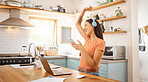 Young beautiful cheerful mixed race businesswoman holding and using a phone while wearing headphones and listening to music working from home. One joyful hispanic woman using social media on her cellphone and enjoying a music break
