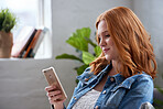 Beautiful redhead woman using smartphone texting browsing messages on mobile phone relaxing at home